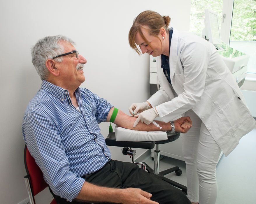 Ärztin entnimmt einem älteren Mann eine Blutprobe in einer Arztpraxis